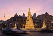 Golden Christmas decorations in Baku with historic architecture and modern Flame Towers at sunset.