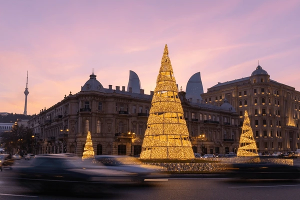 Golden Christmas decorations in Baku with historic architecture and modern Flame Towers at sunset.